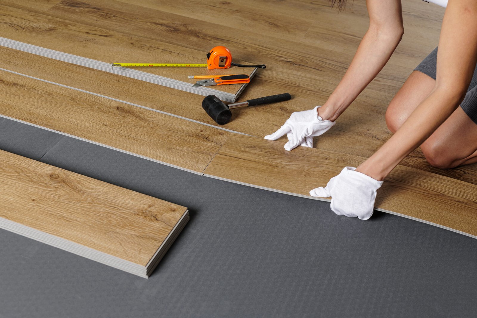 Close view of female installer fitting SPC vinyl planks with click lock and tools on underlayment for home upgrade